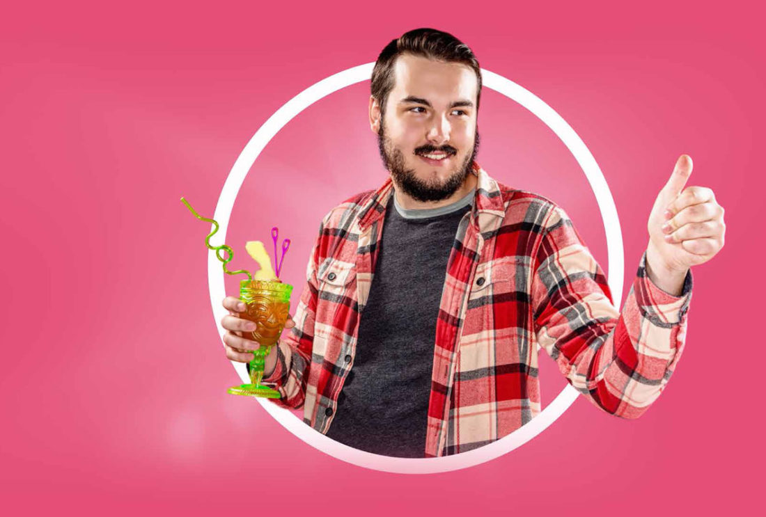 man with beard and moustache wearing plaid shirt and holding cocktail with twirly straw and umbrella, he is giving the thumbs up with his other hand
